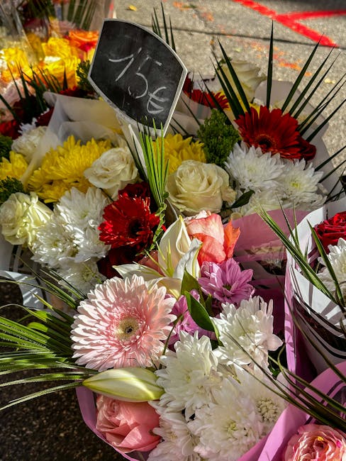 A vibrant flower arrangement featuring a variety of fresh blooms, including large white roses, red gerbera daisies, soft pink gerbera daisy, white carnations, and purple chrysanthemums, all set in pin