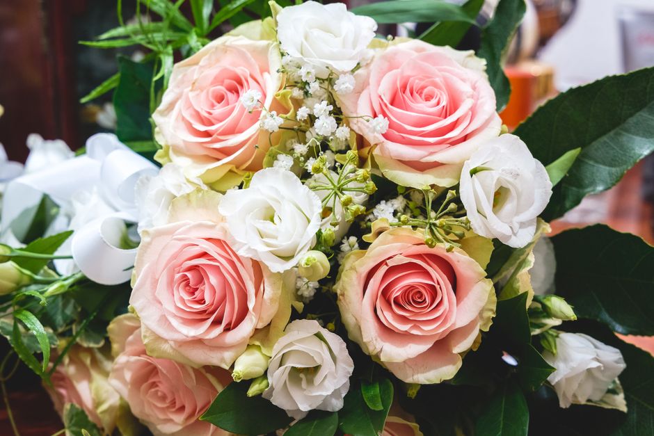 A close-up of a floral arrangement featuring a bouquet of fresh pink and white roses, complemented by small white filler flowers and lush green foliage. The roses exhibit delicate, velvety petals arra
